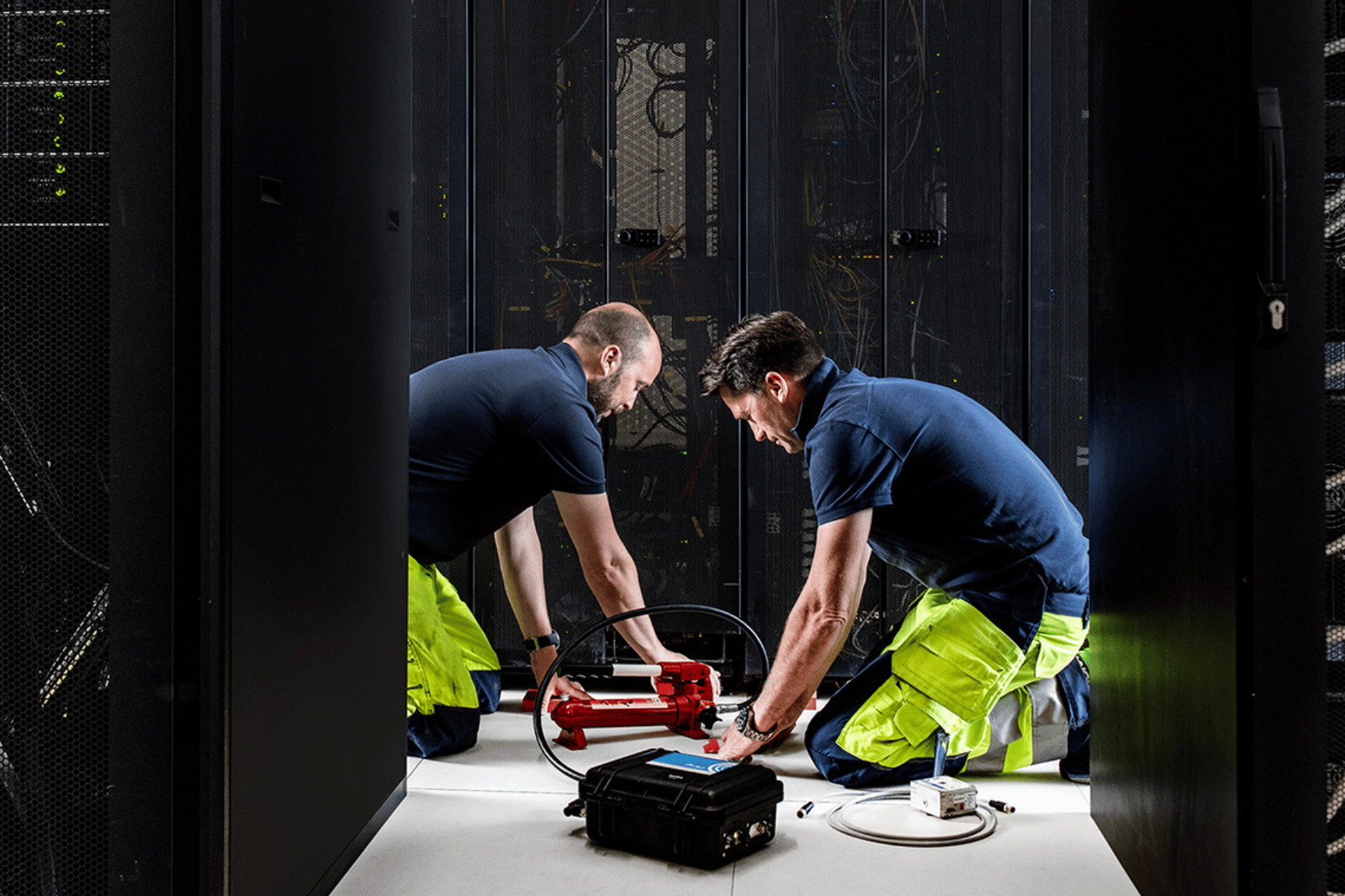 Bildet viser to ansatte i ProTech Consult som monterer inn vibrasjonsdempere på et serverskap/datarack. 